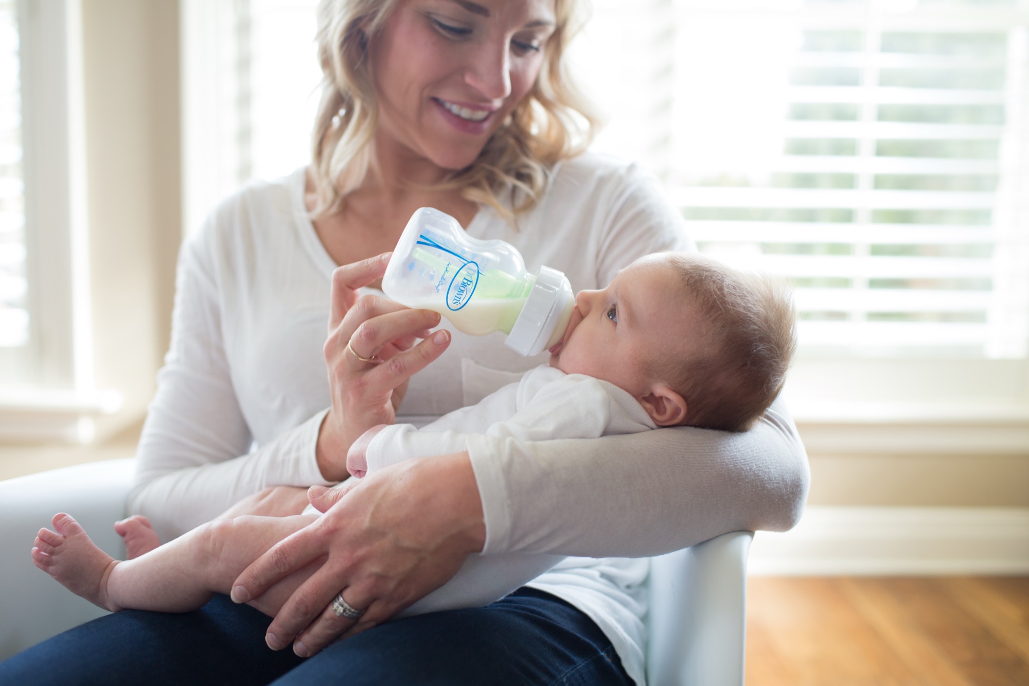 Mamá dando mamadera Dr. Brown's Options+ a su bebé junto a la ventana en momento de calma