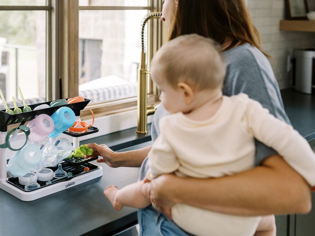 Mamá con su guagua en brazos junto al rack de secado Dr. Brown's cargado, en la cocina